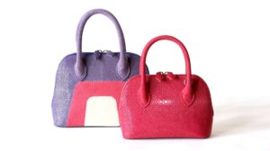 Two luxury stingray leather handbags in purple and red with textured finishes and top handles from AKNAS