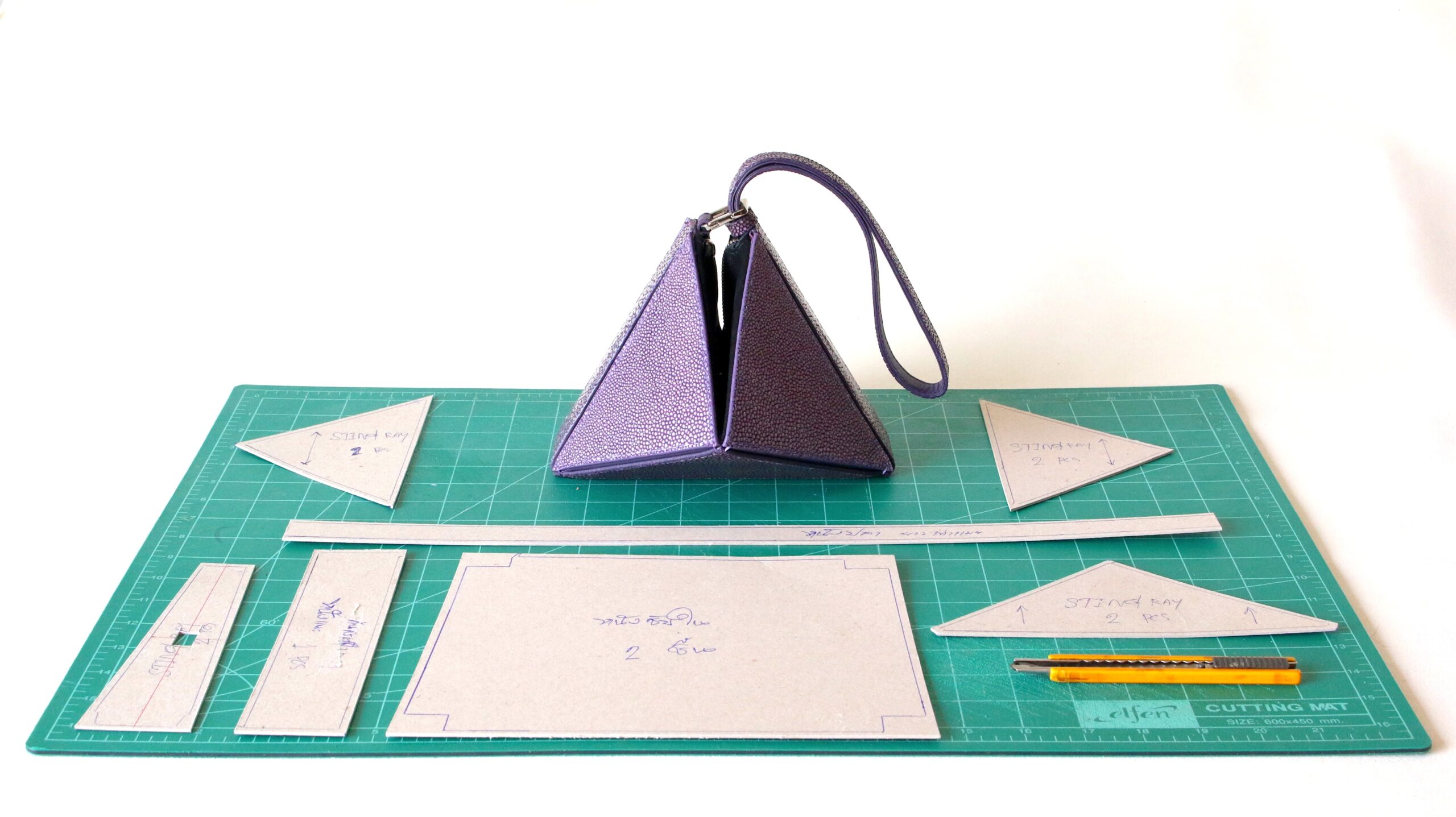 ODM handbag development: purple triangular wristlet prototype displayed with cardboard cutting patterns and tools on a green cutting mat.