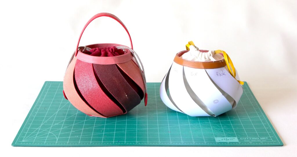 Red stingray leather bucket handbag with a rounded top handle displayed next to a white handbag prototype from AKNAS