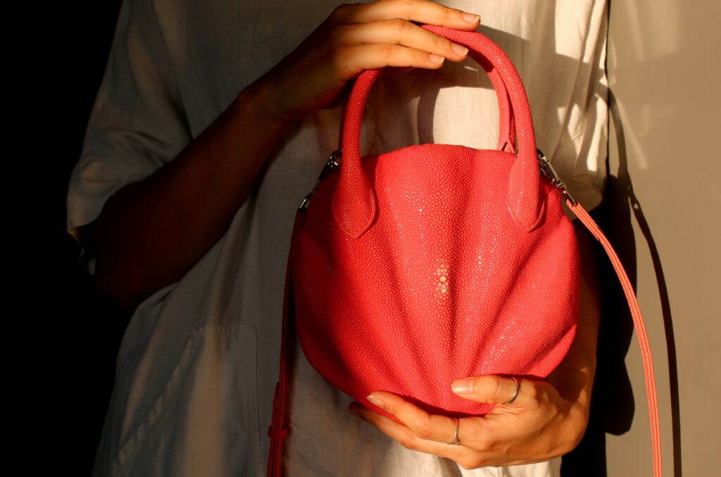 Custom coral pink stingray leather mini bag developed with AKNAS, featuring a sculpted design, rounded top handles, and detachable shoulder strap.