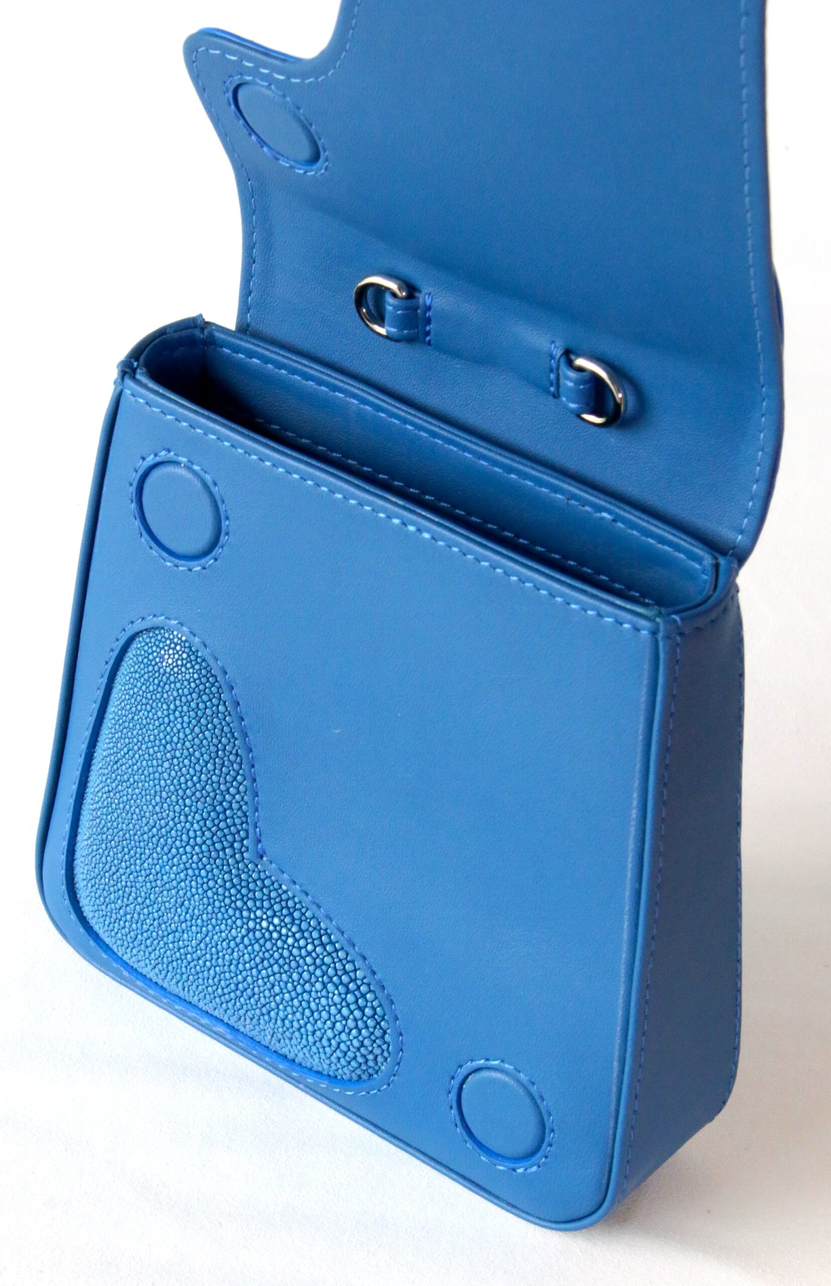 Open blue leather handbag with a textured stingray leather heart-shaped detail, flap closure, and silver metal hardware.