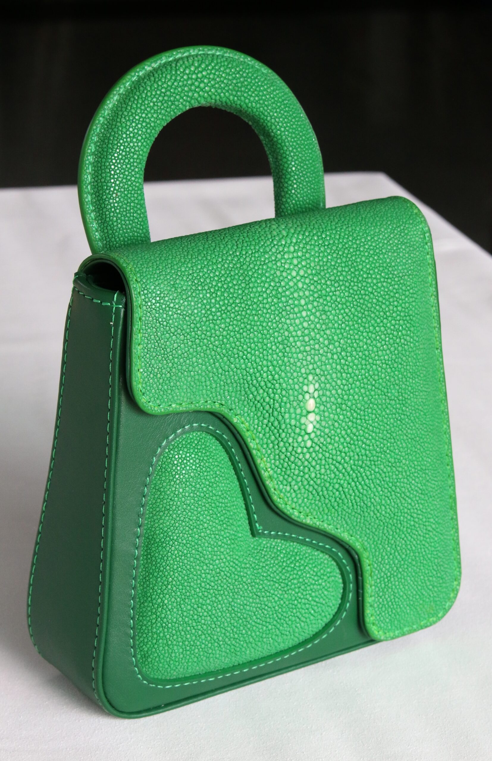 Luxury green stingray leather handbag with a structured top handle, textured finish, and decorative heart-shaped side panel.