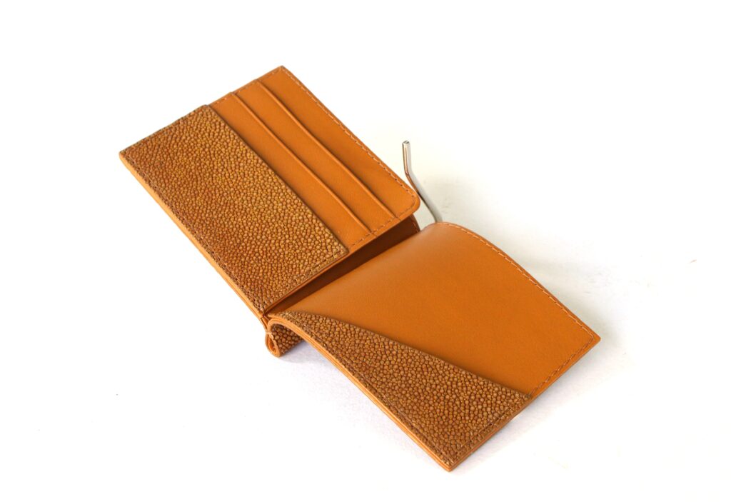 Open orange stingray leather bifold wallet by AKNAS featuring textured panels, card slots and a money clip.